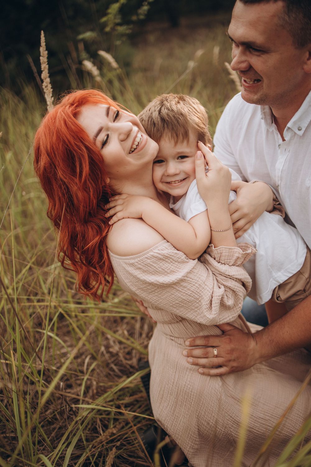 A joyful family moment captured in a field with tall grass showing genuine smiles and embraces.