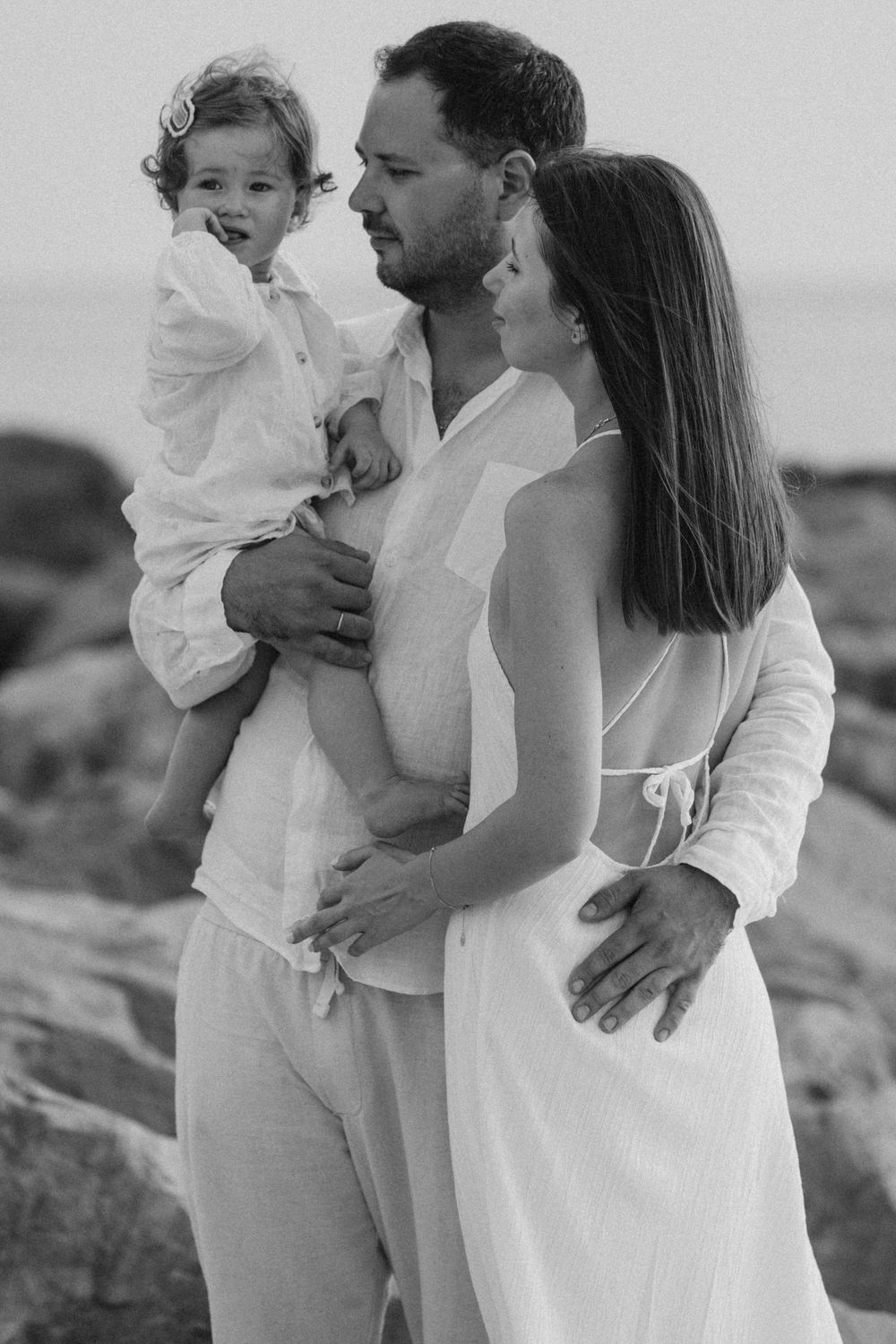 A serene black and white family portrait captured against a coastal backdrop.