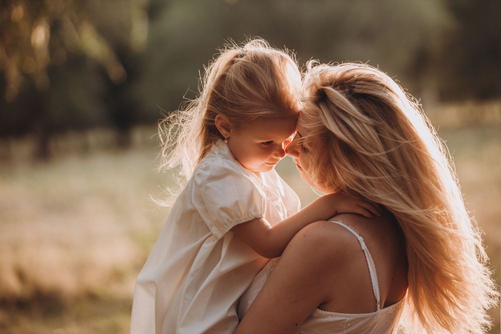 Tender moment between mother and child in sunlit outdoor setting.
