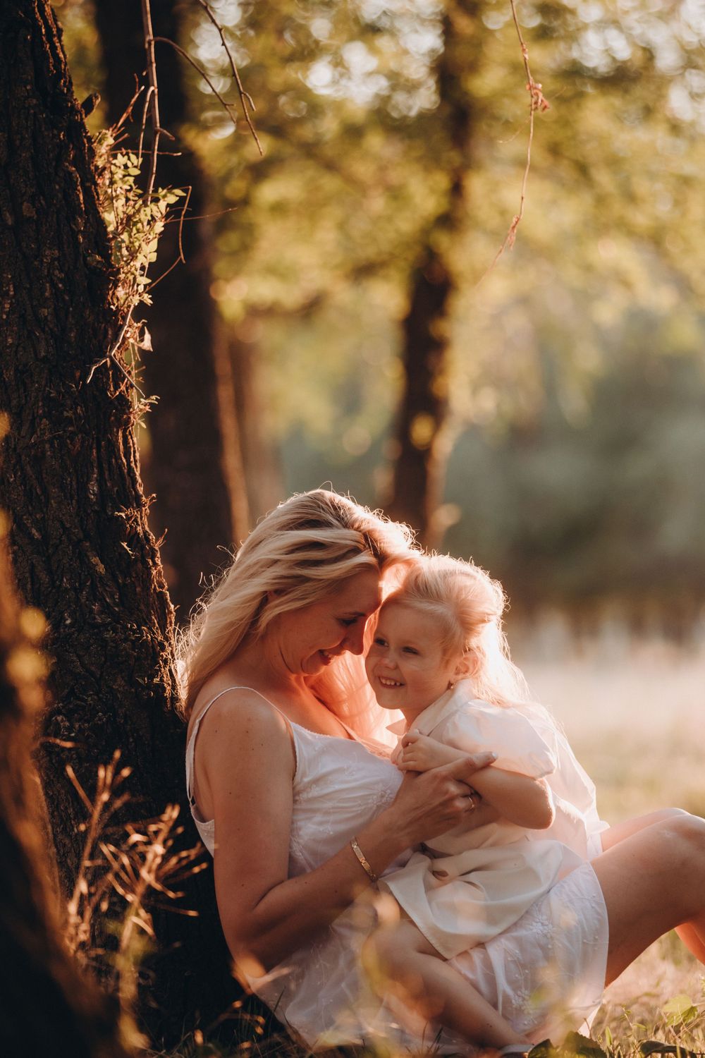 A tender moment between parent and child sitting beneath a tree at sunset.