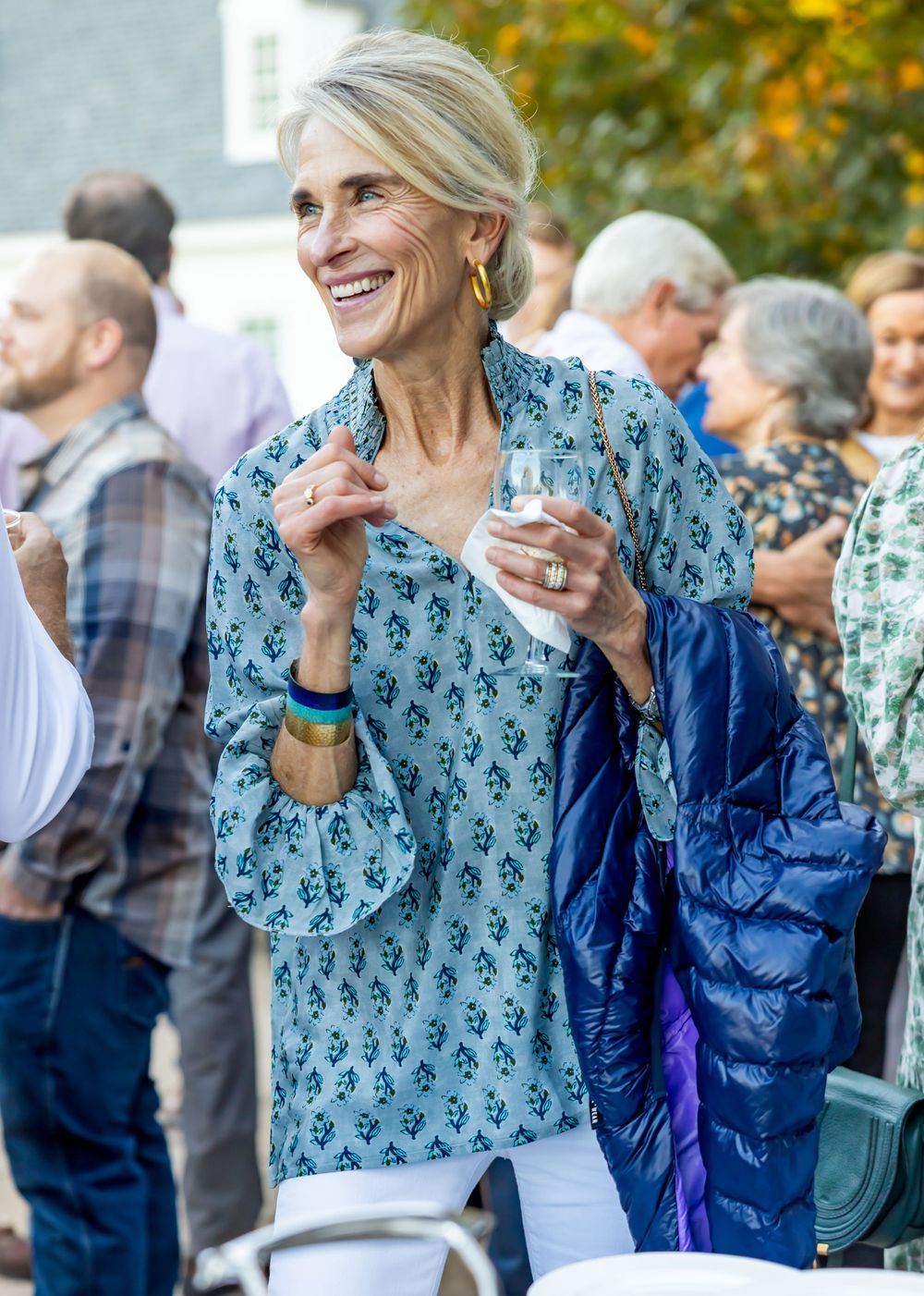 Woman in patterned blue top smiling while holding drink at outdoor party.