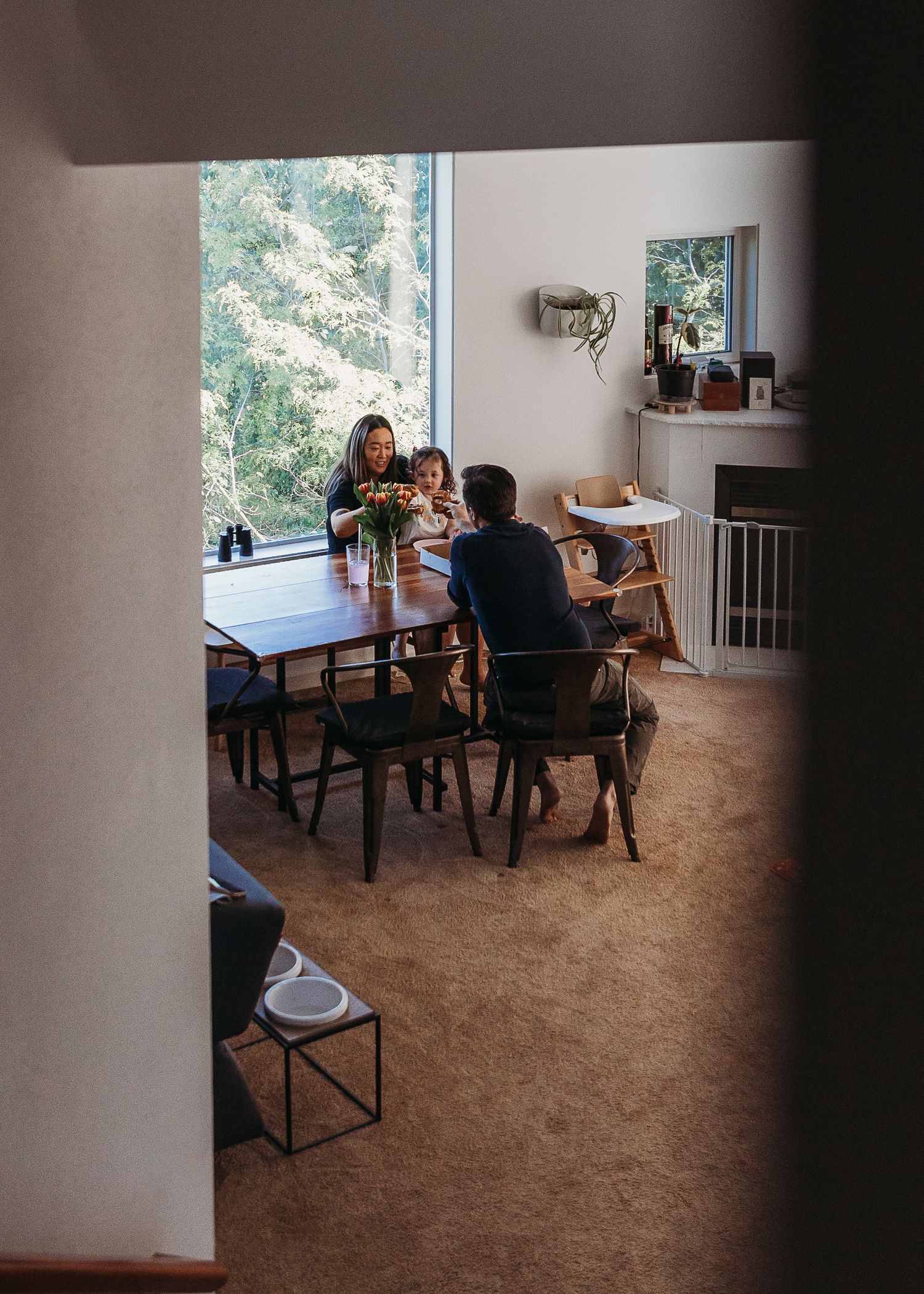 Family gathered around a wooden dining table with large windows overlooking nature.