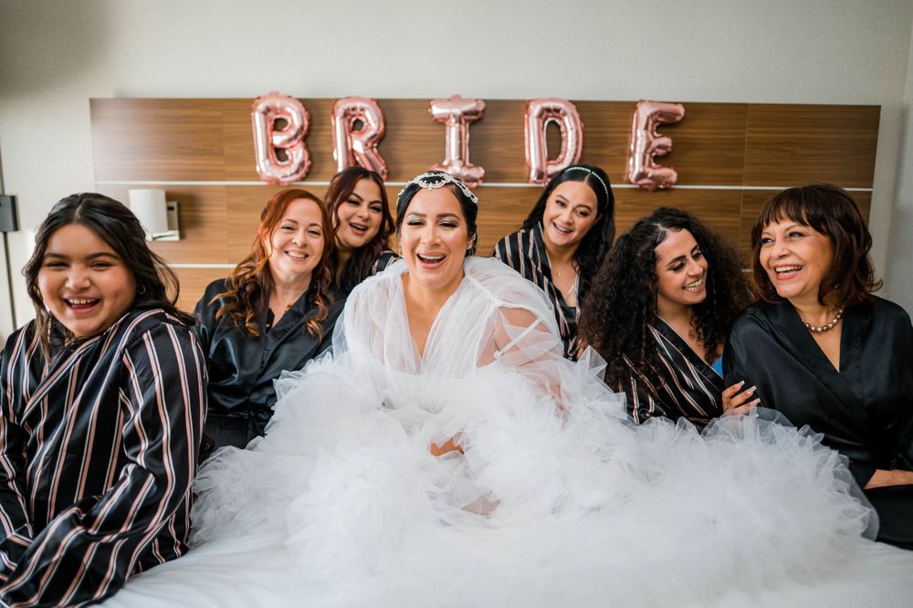 Wedding party gathered on hotel bed with the bride in a flowing white dress.