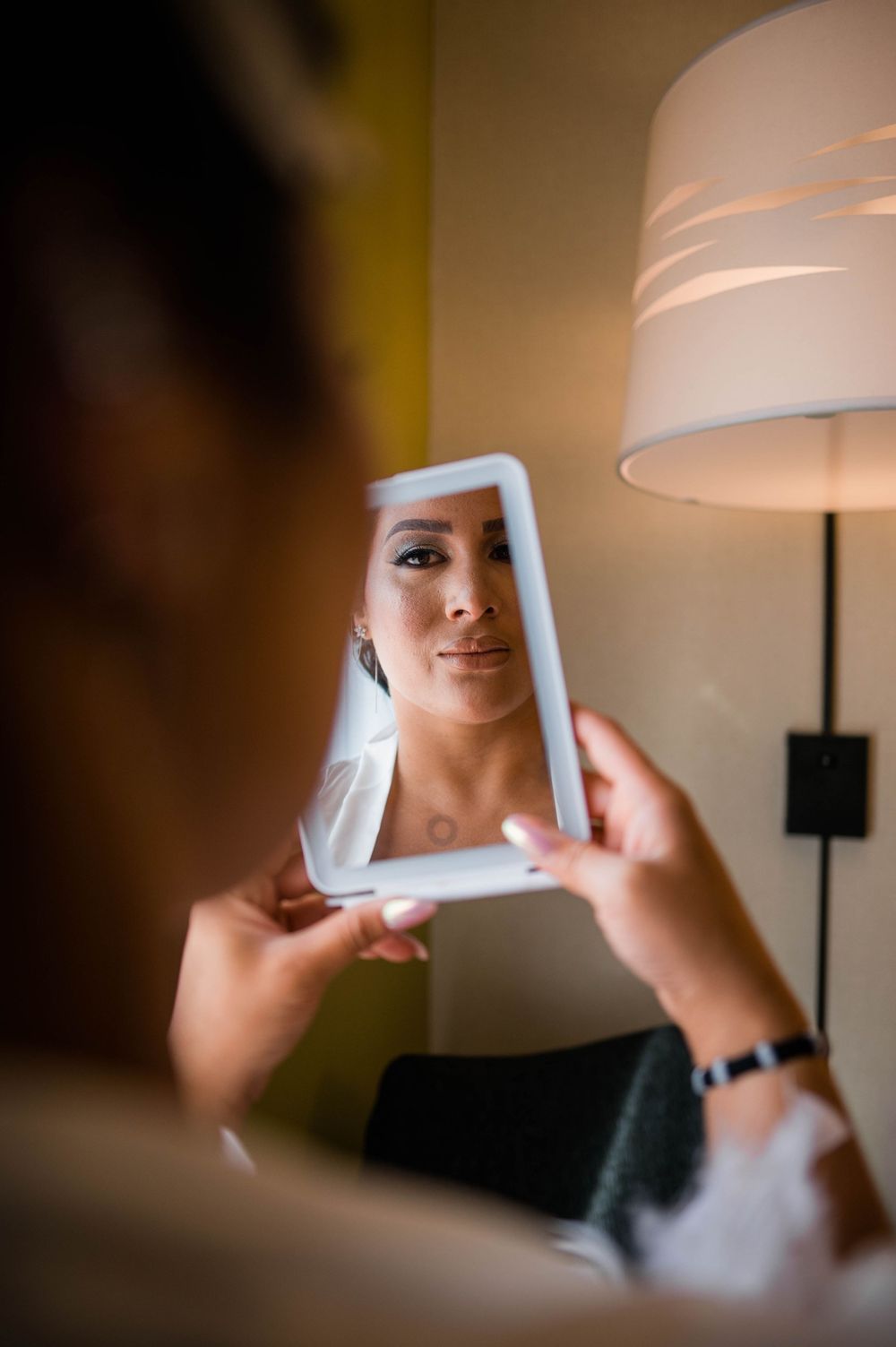 Hand holding small mirror during bridal makeup session.
