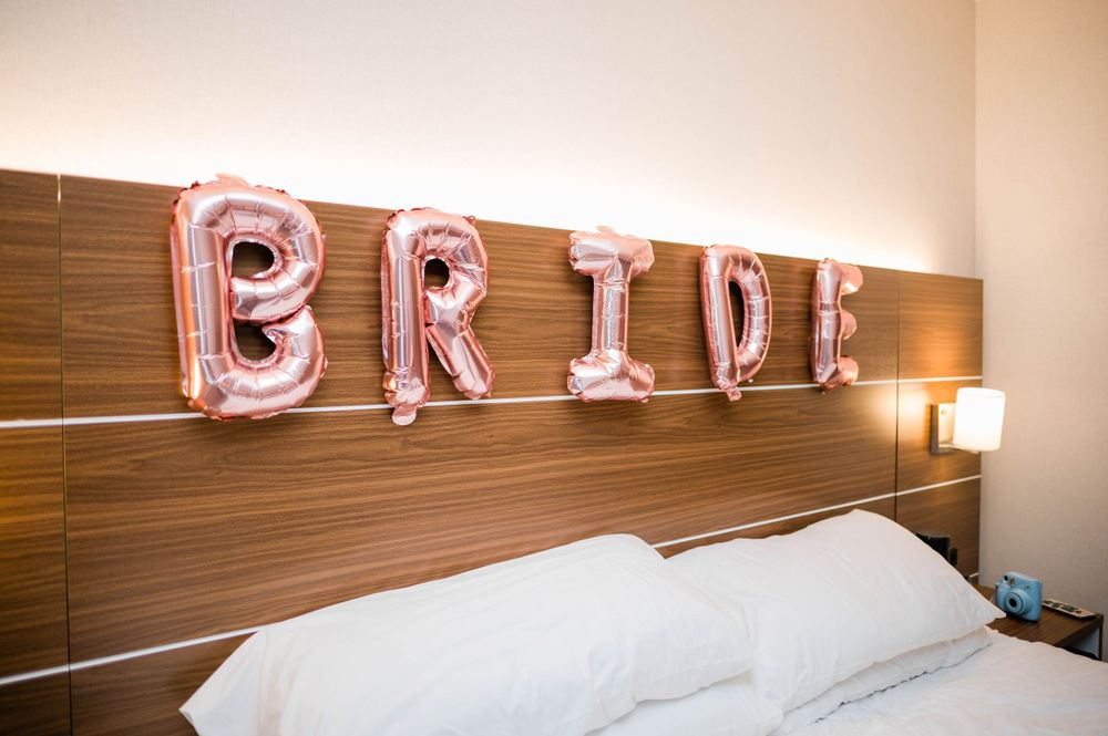 Pink foil balloon letters spelling 'BRIDE' mounted on wooden hotel headboard.