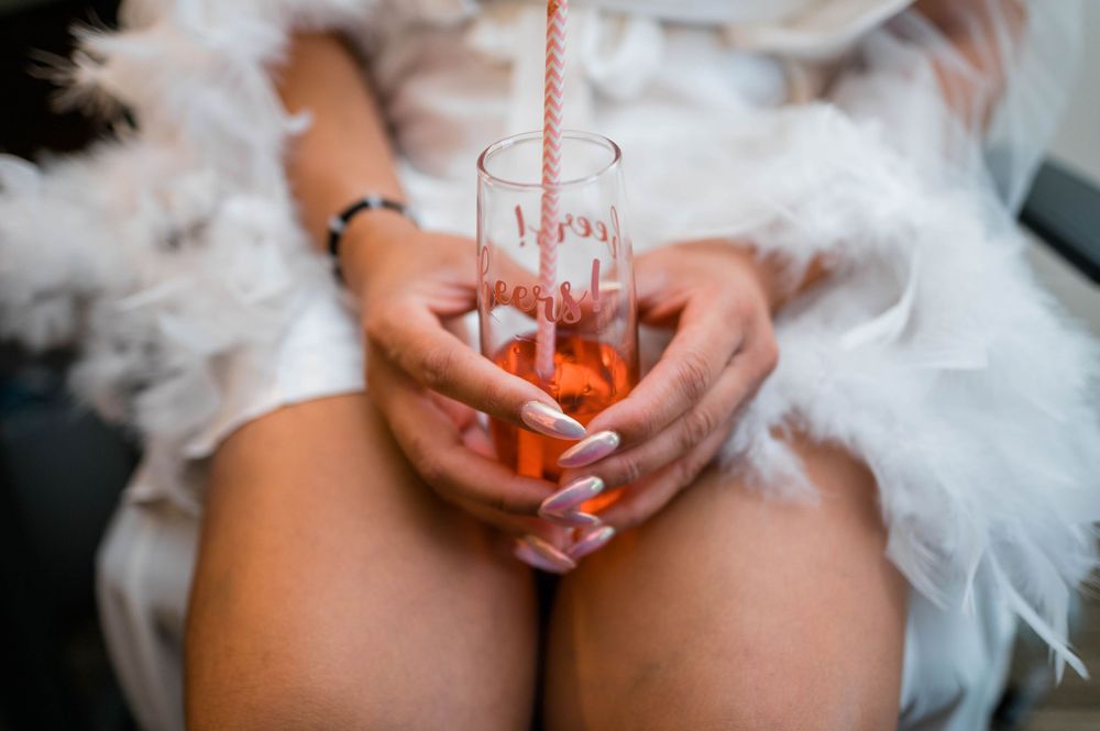Close up of hands holding pink cocktail with straw against white fabric.