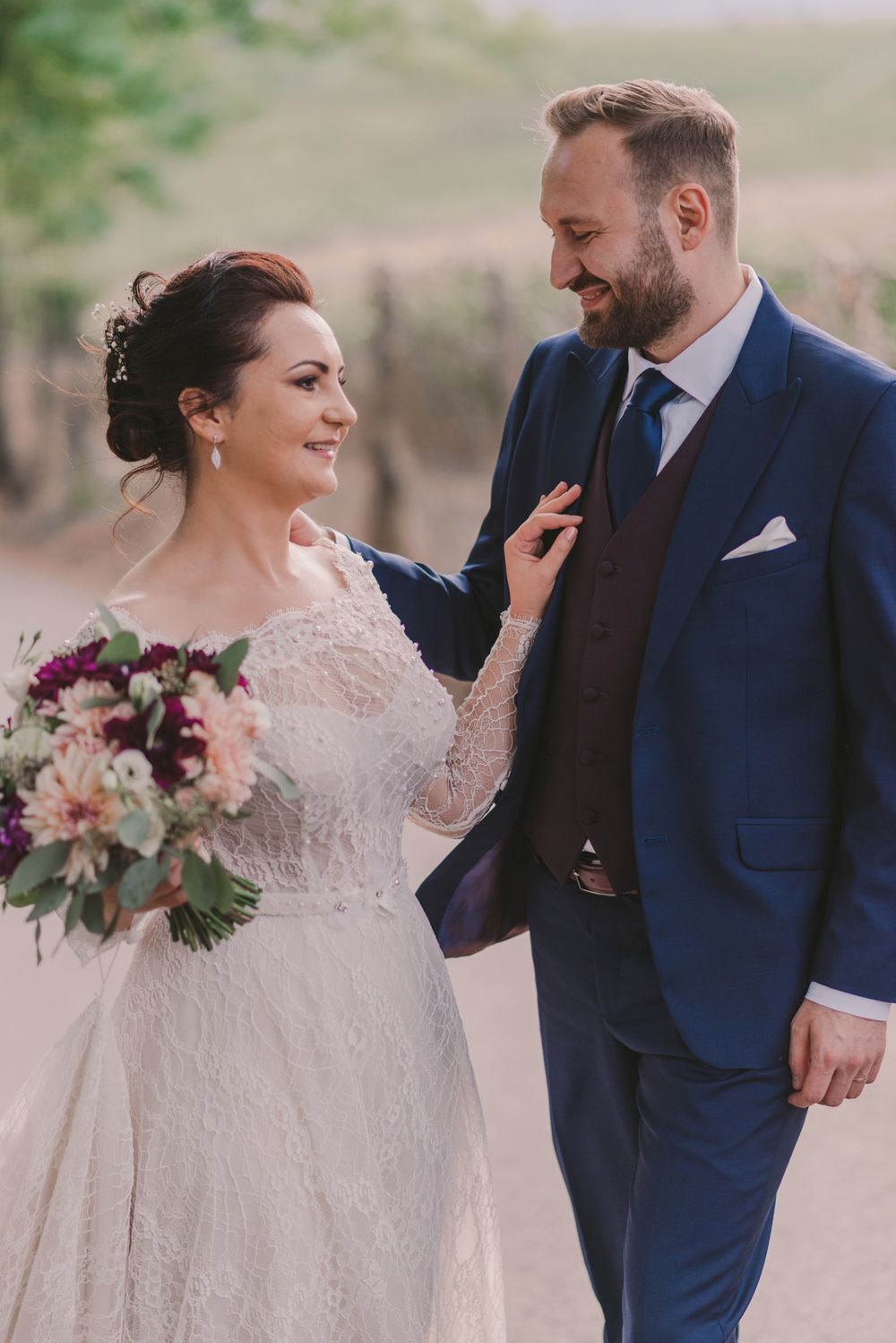 Romantic outdoor portrait of newlyweds with pink floral bouquet.