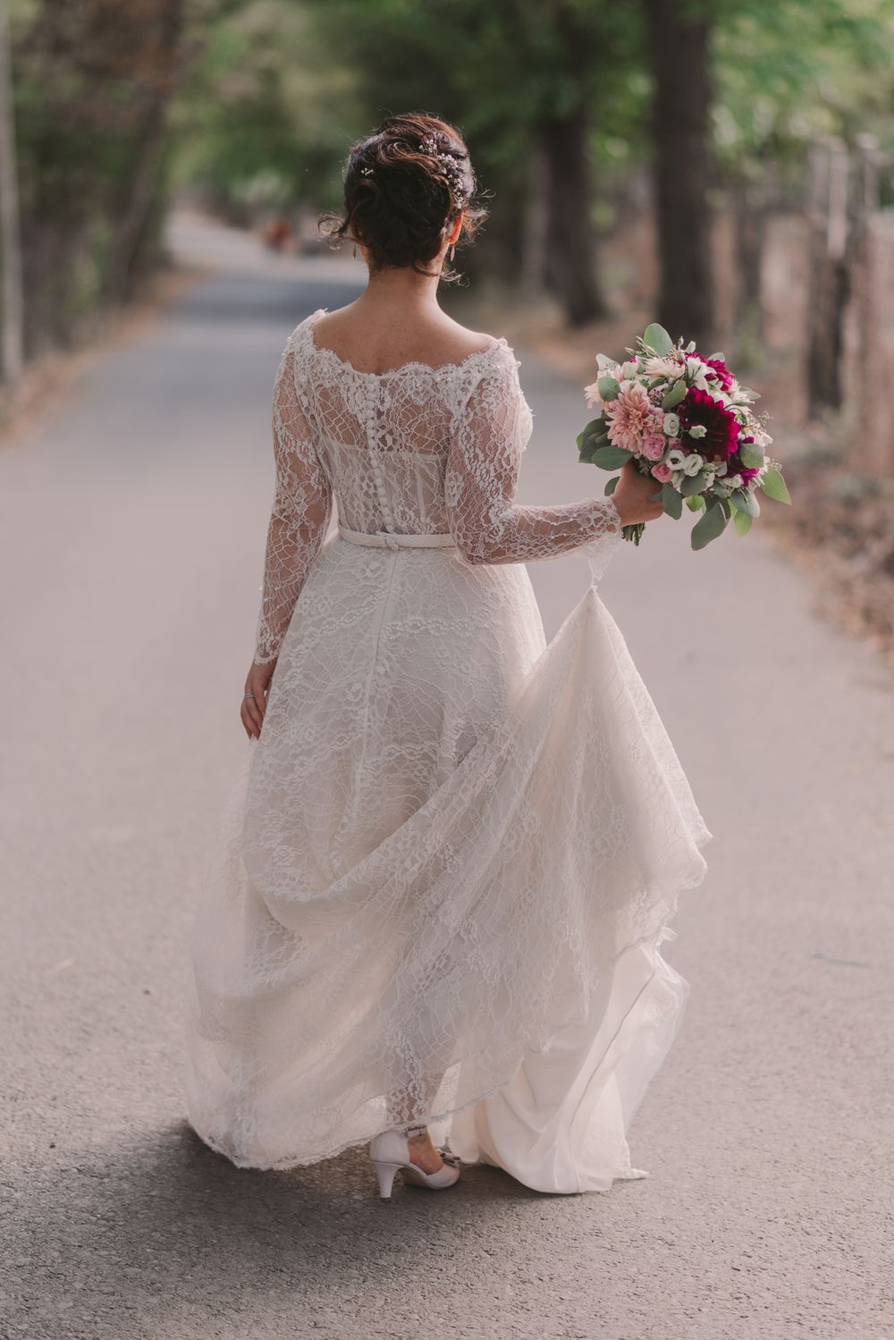 Elegant lace wedding dress with long sleeves flows beautifully on a wooded path during a bridal photoshoot.