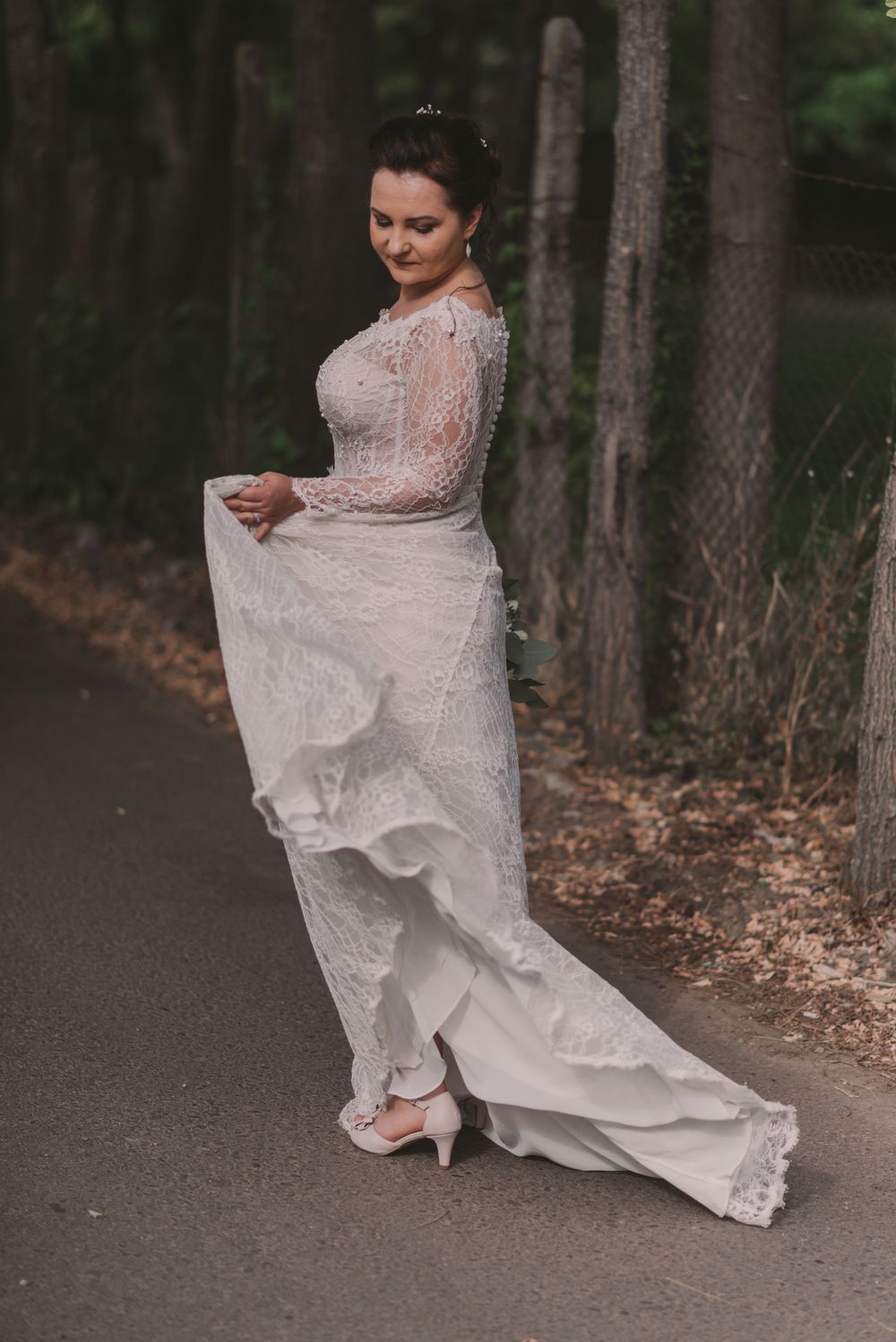 Romantic bridal portrait showing the delicate details of a lace wedding gown from behind on a forest path.