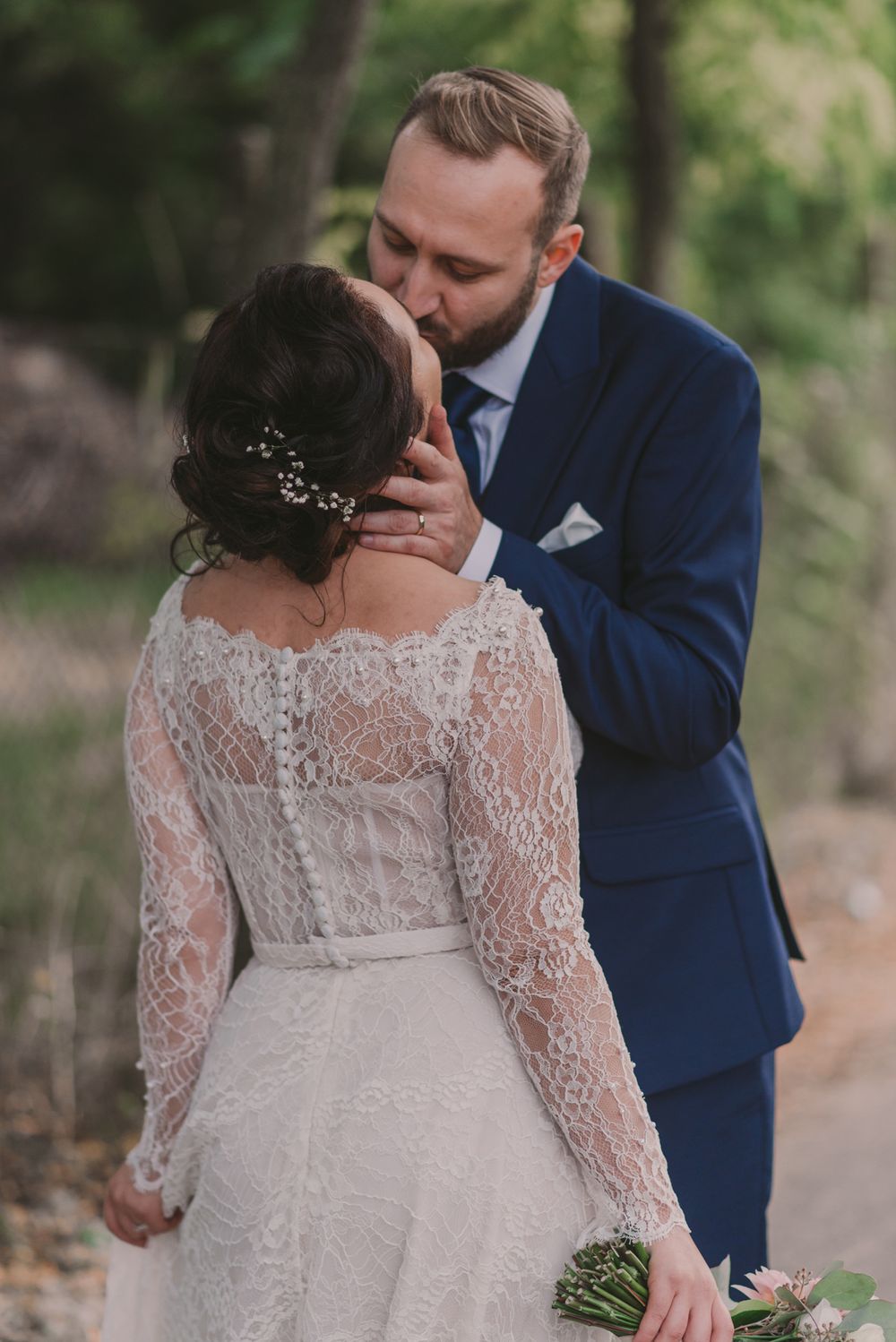 Wedding couple shares tender moment outdoors with bride in long-sleeve lace gown.
