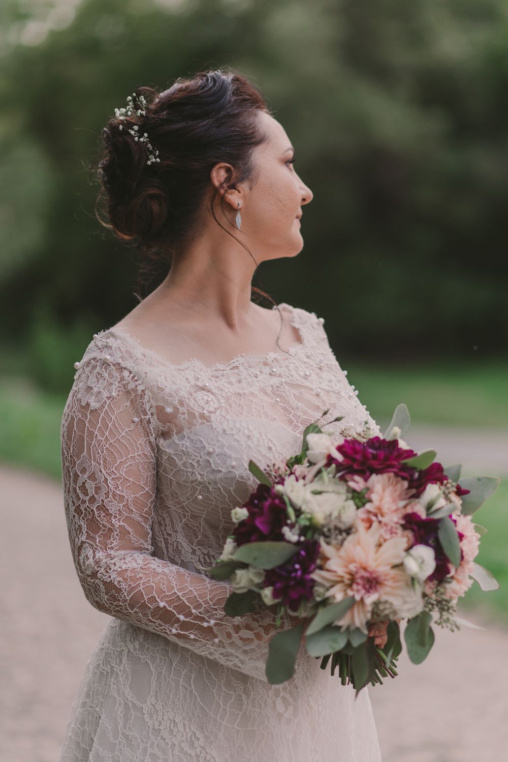 Bride holds stunning bouquet of pink and purple flowers while wearing detailed lace sleeve wedding dress.