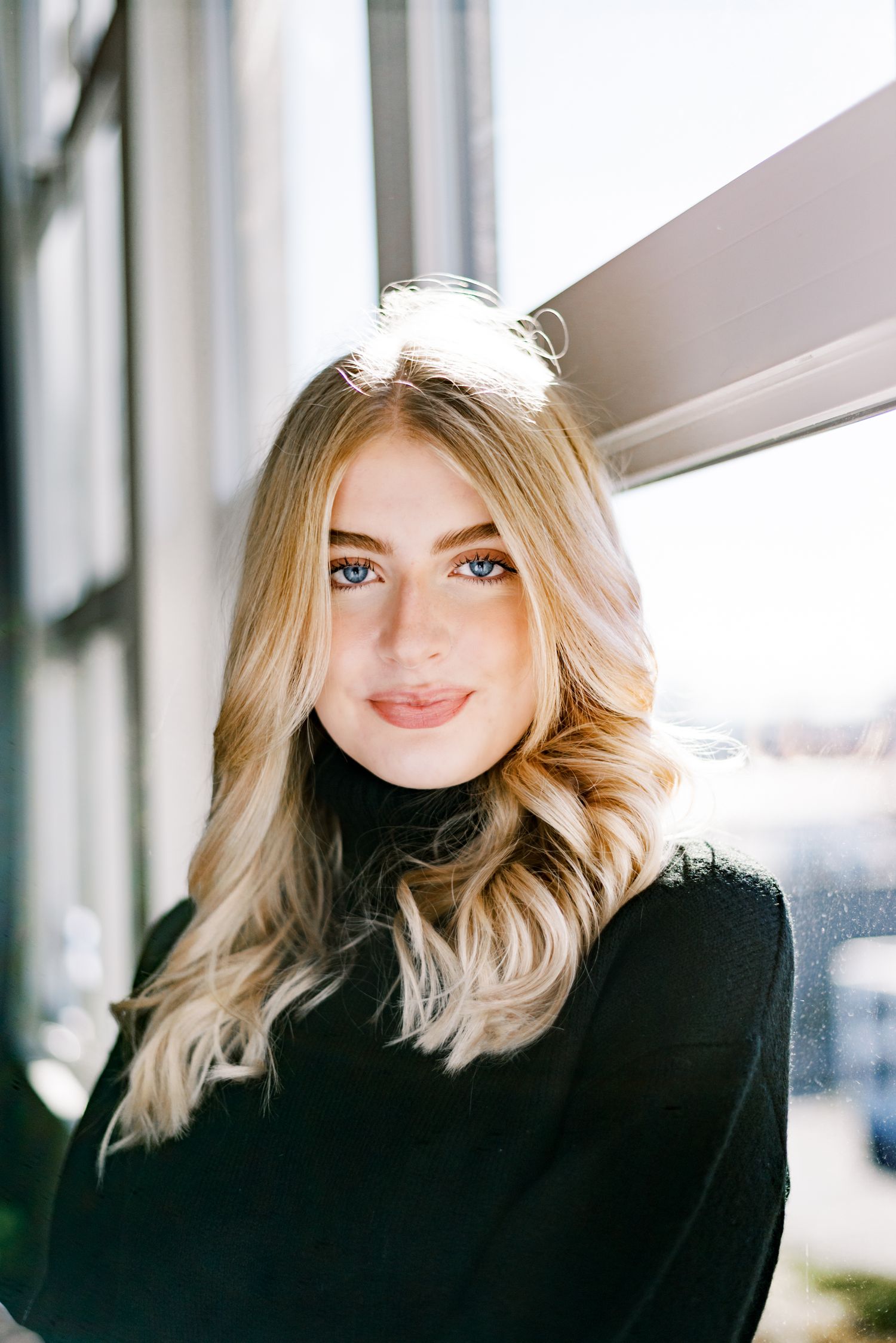 Portrait of woman in black turtleneck with blonde wavy hair against white background.