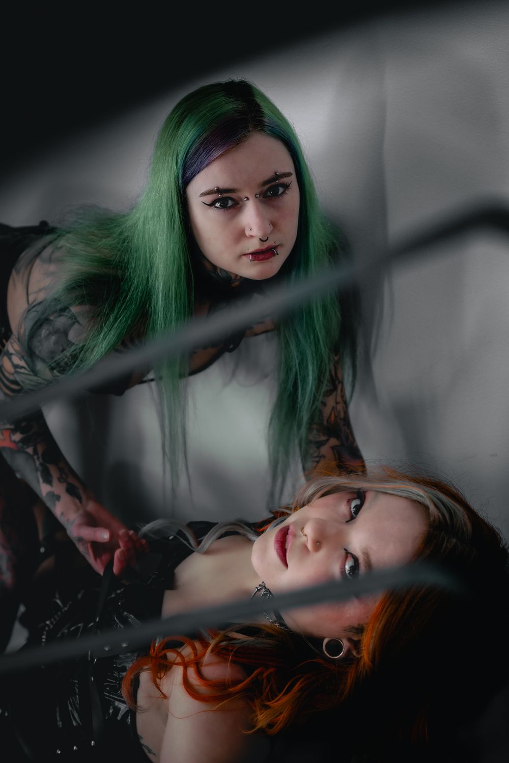 Green-haired woman stands on top orange-haired woman on stairs, both wearing lingerie and gazing fiercely at the camera in Gatineau, Quebec.