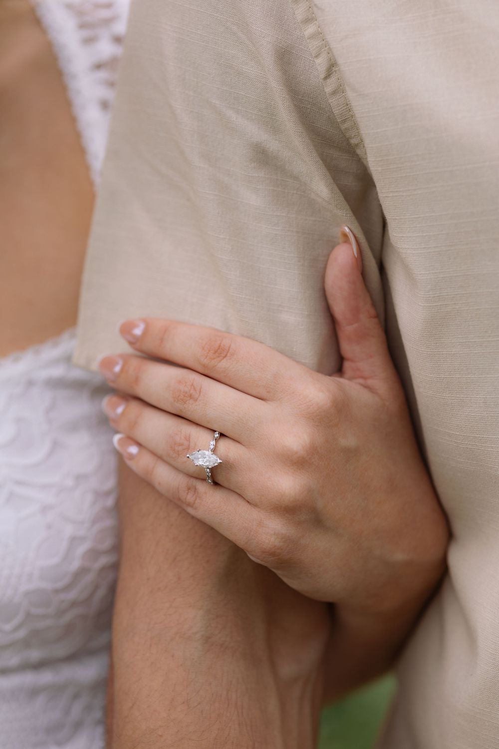 Close-up of a marquise diamond engagement ring on a woman's hand resting on a man's chest.