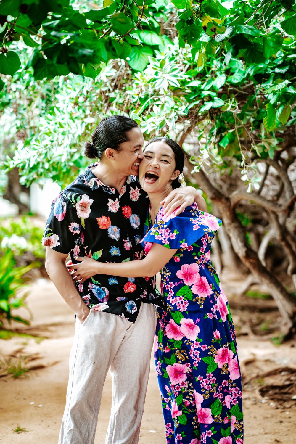 Joyful couple in coordinating floral outfits sharing a laugh in a lush garden setting.