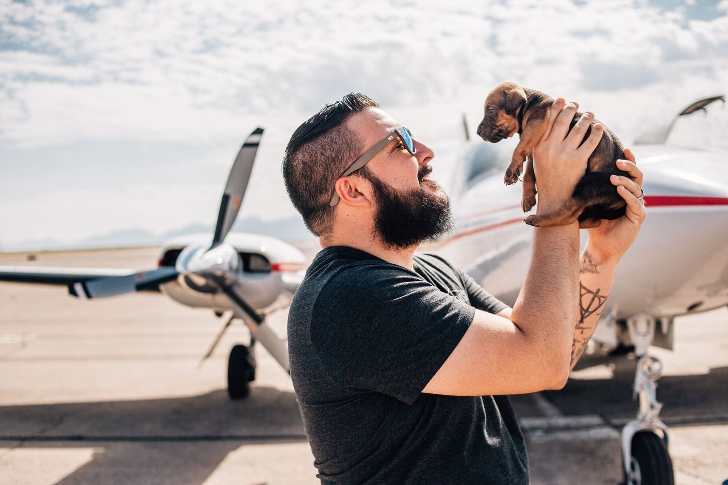 man hold puppy up with plane in the background