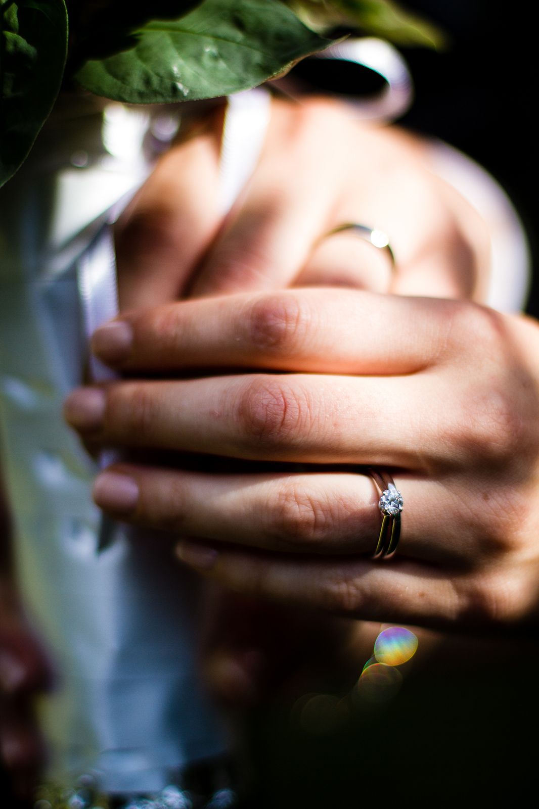 Close-up of hands holding flowers with engagement ring visible.