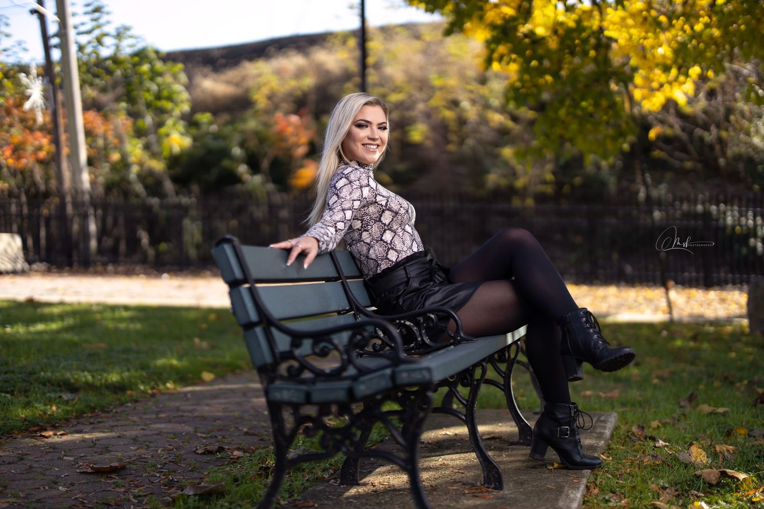 Outdoor autumn portrait of person sitting on park bench surrounded by fall foliage.