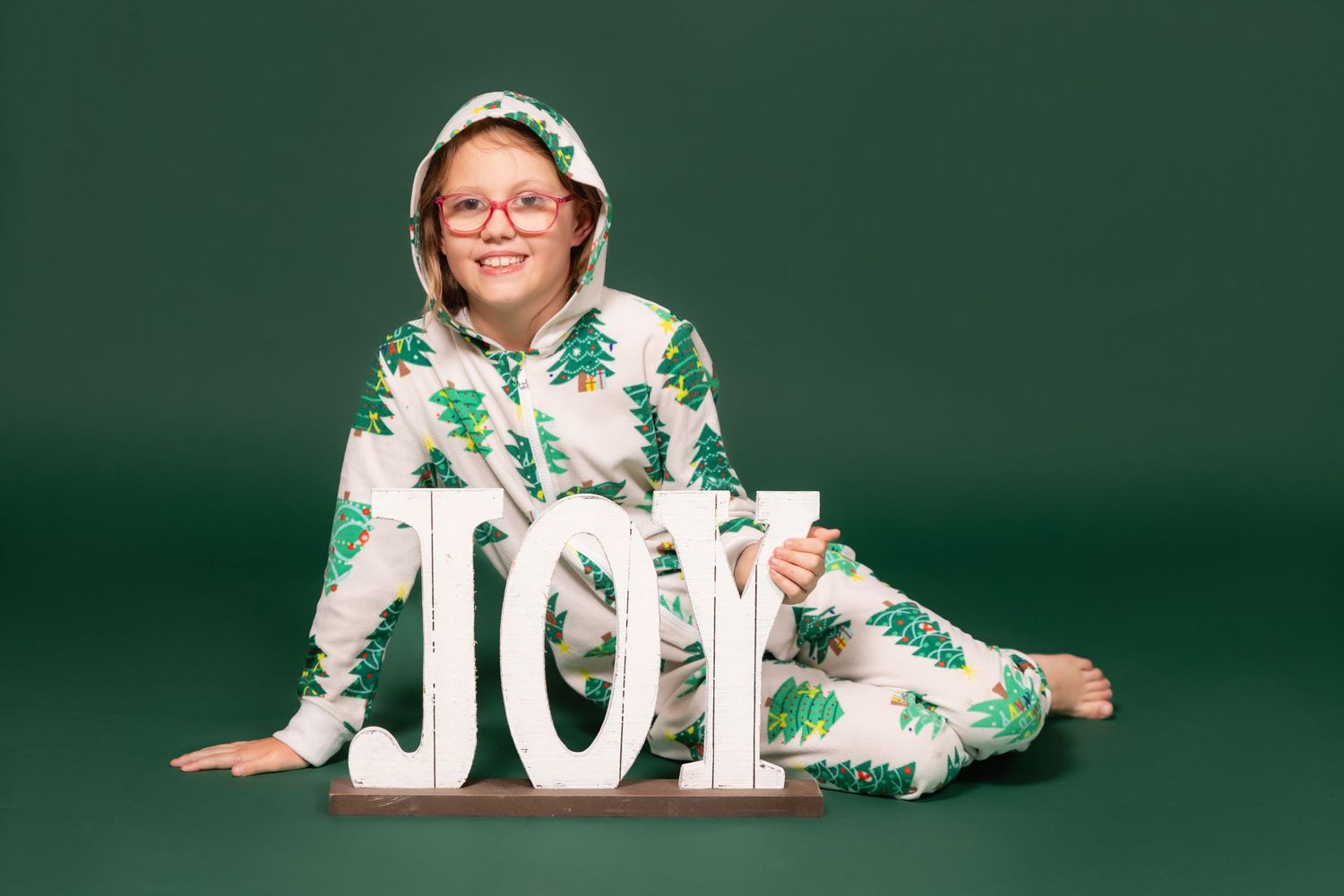 child in christmas tree pajamas with joy sign on solid green backdrop in studio clayton new jersey Gloucester