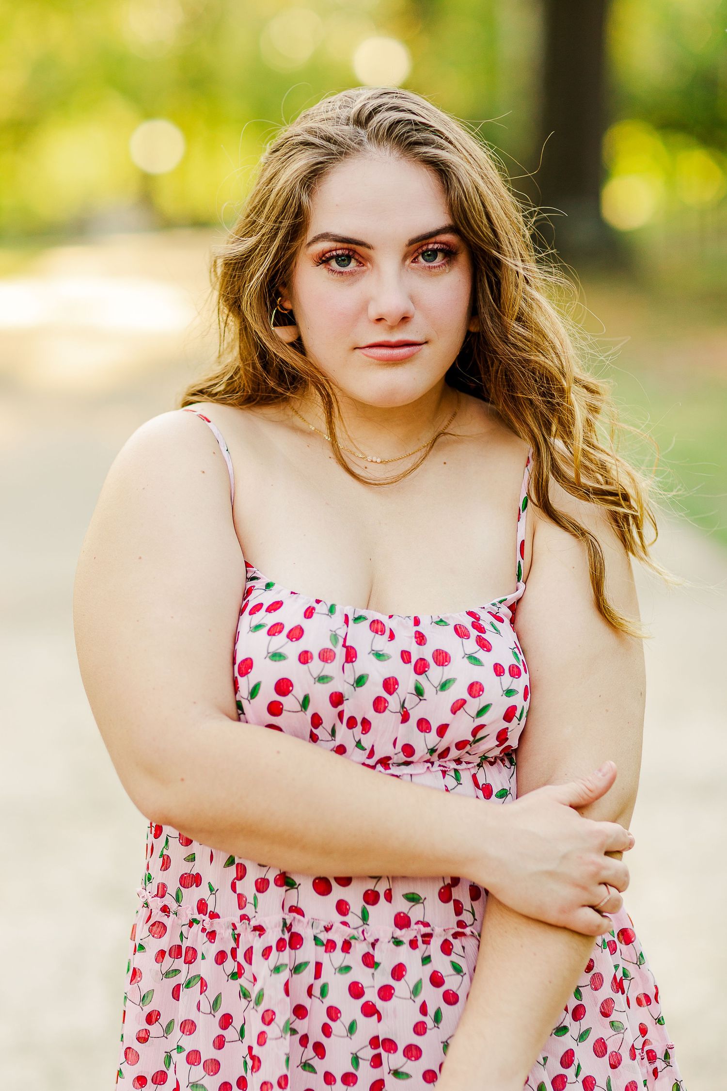 Graduate poses in cherry print sundress outdoors during photo session.