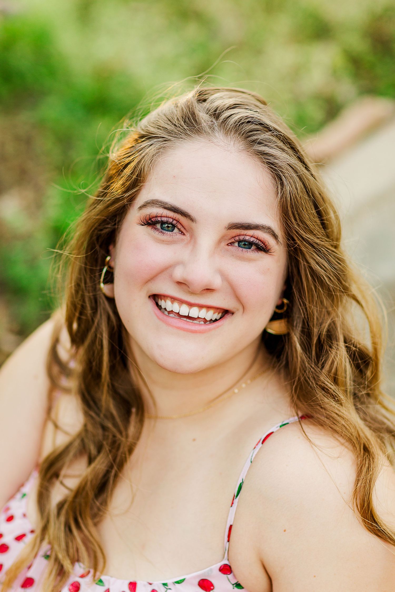 Portrait of graduate in floral sundress smiling outdoors on sunny day.