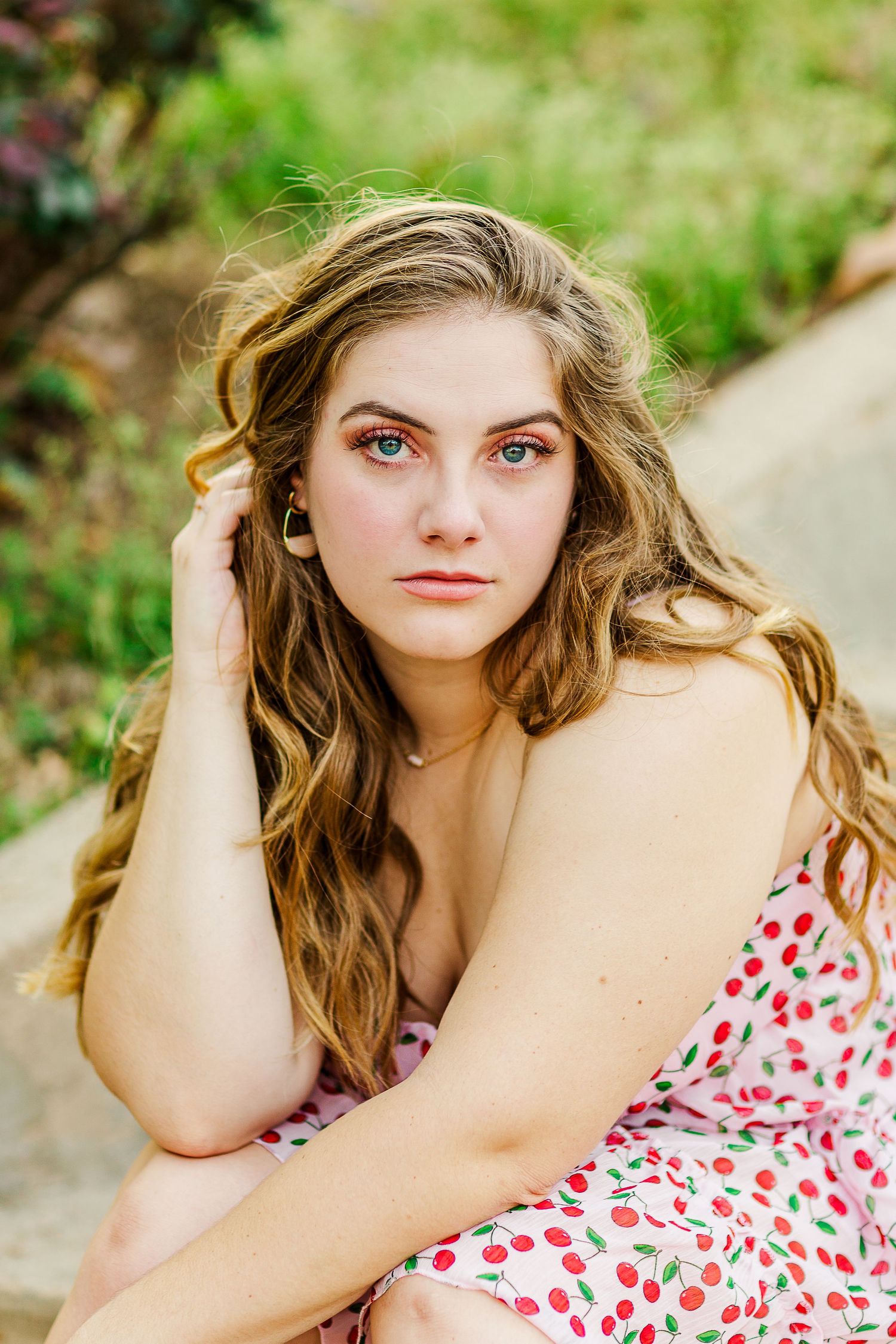 Portrait of graduate in floral dress sitting outdoors with wavy hair against natural background.