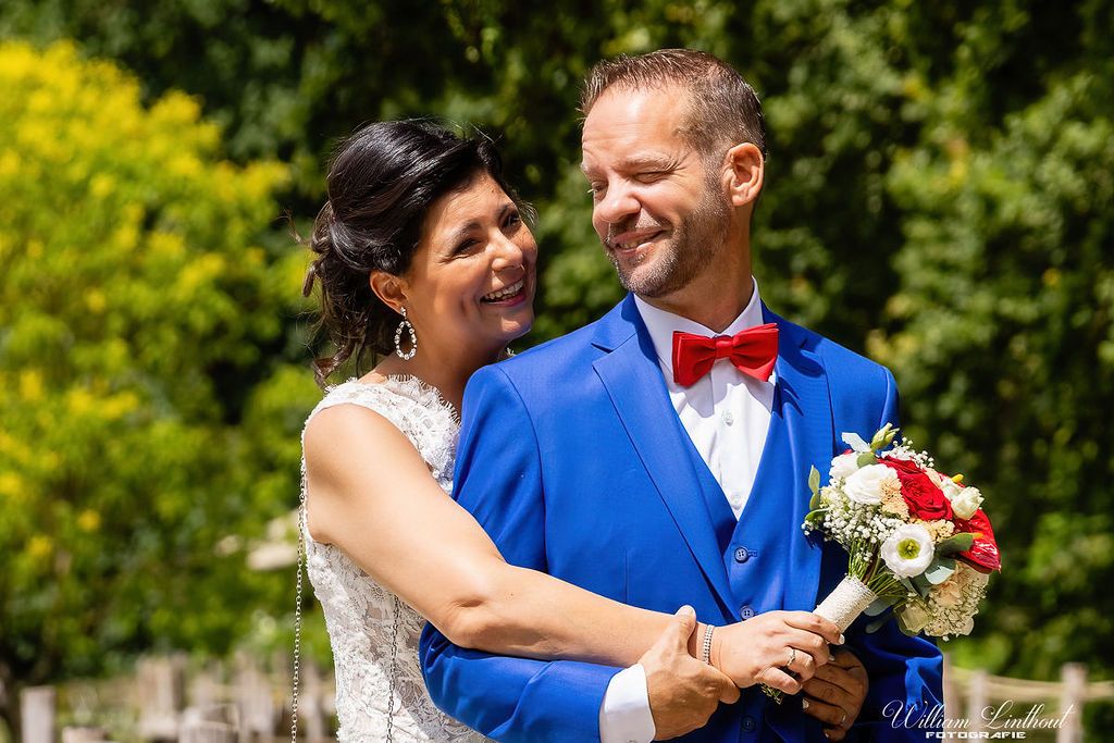 A couple shares a joyful moment outdoors with the groom wearing a striking blue suit and red bowtie.