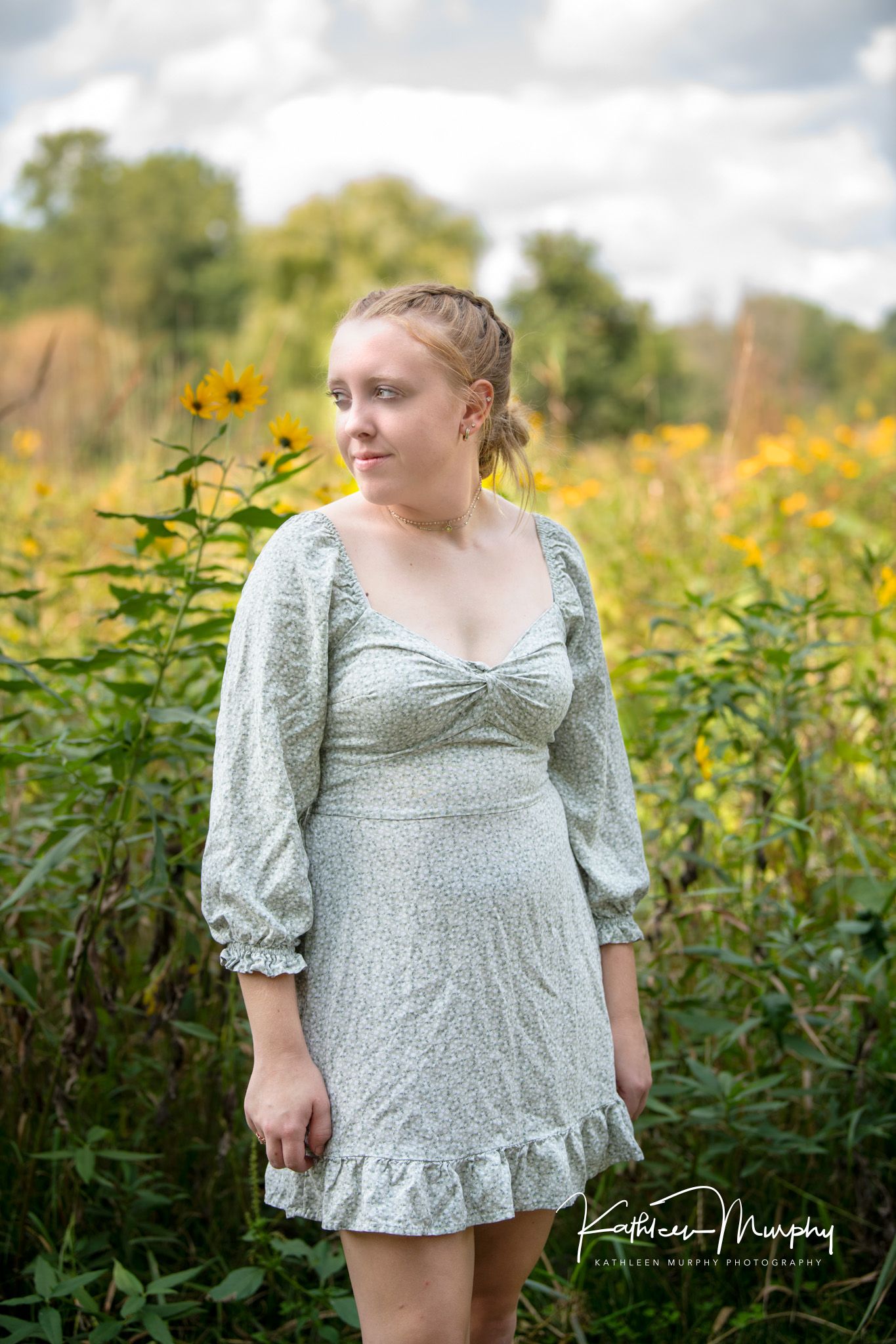 Portrait in a vintage-style sage green dress standing among wildflowers in late afternoon light.