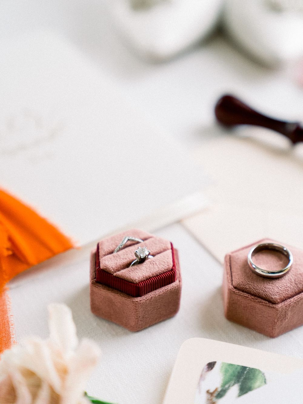 Wedding rings displayed in dusty rose hexagonal ring boxes with orange ribbon accent.