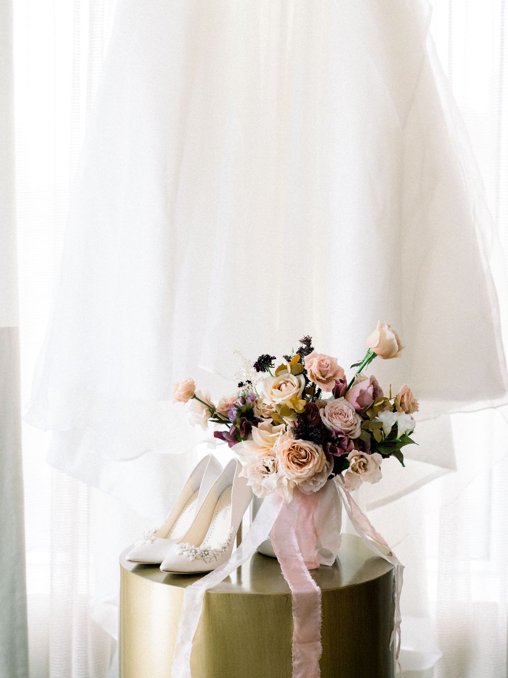 Elegant bridal bouquet with blush roses and white heels on gold pedestal.