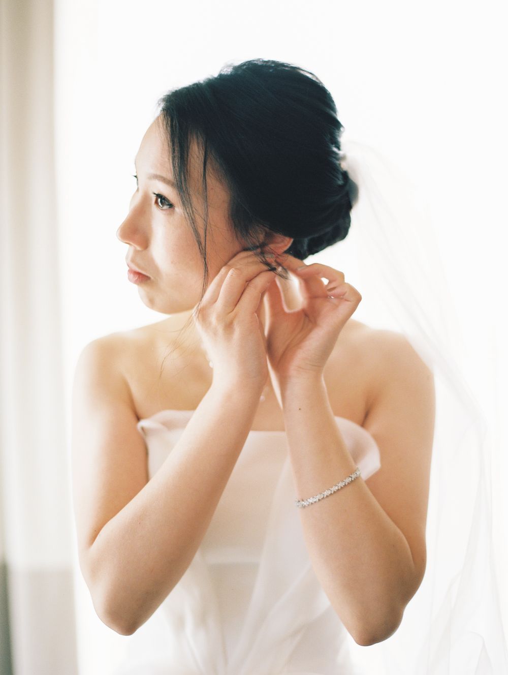 A bride in a strapless white gown puts on earrings while getting ready.