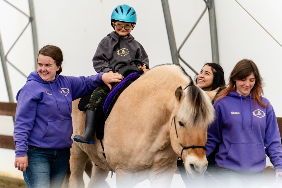 boy smiles while riding a horse with staff and volunteers helping