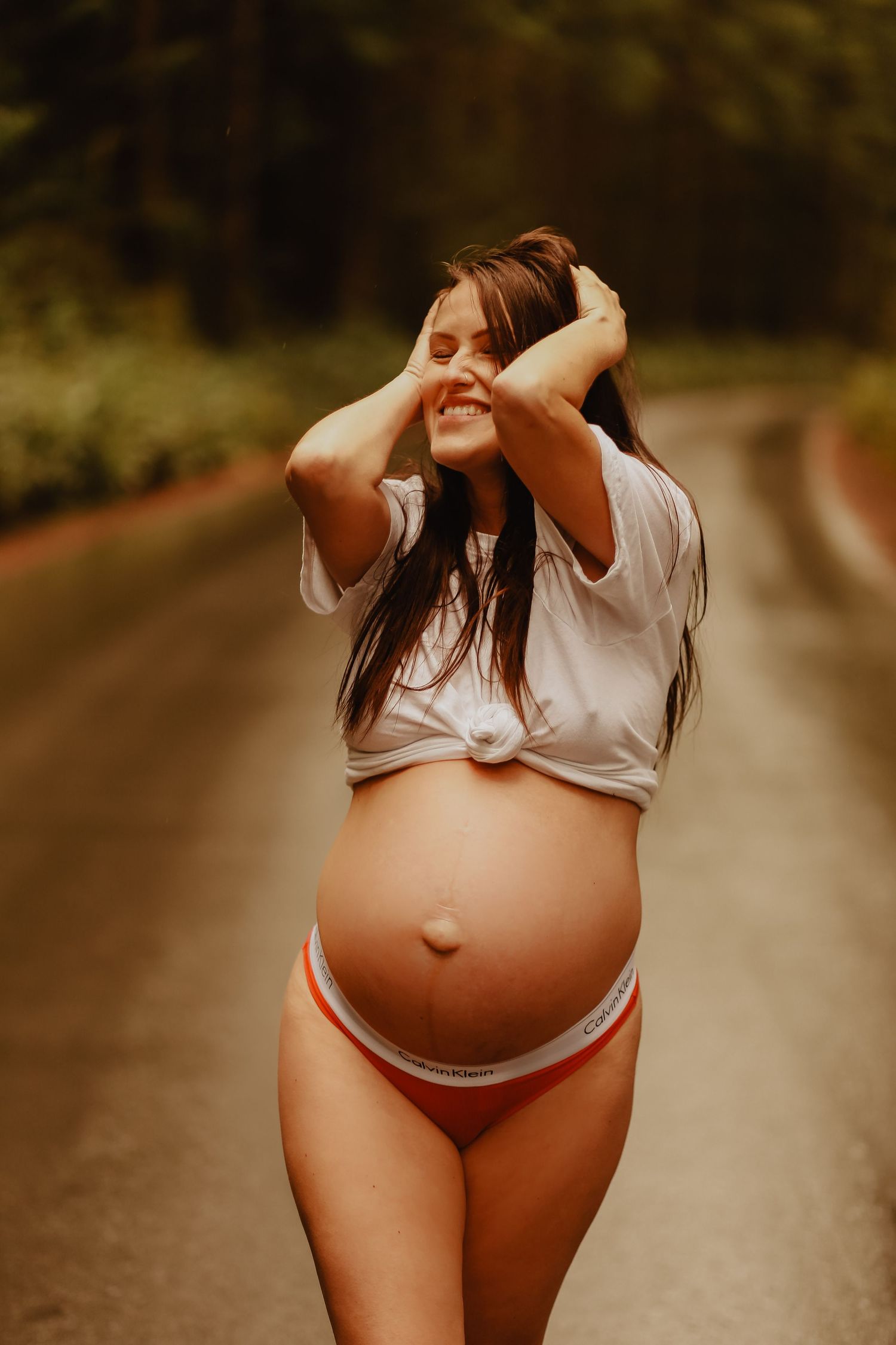 An artistic maternity photo showing a joyful moment on a forest path.