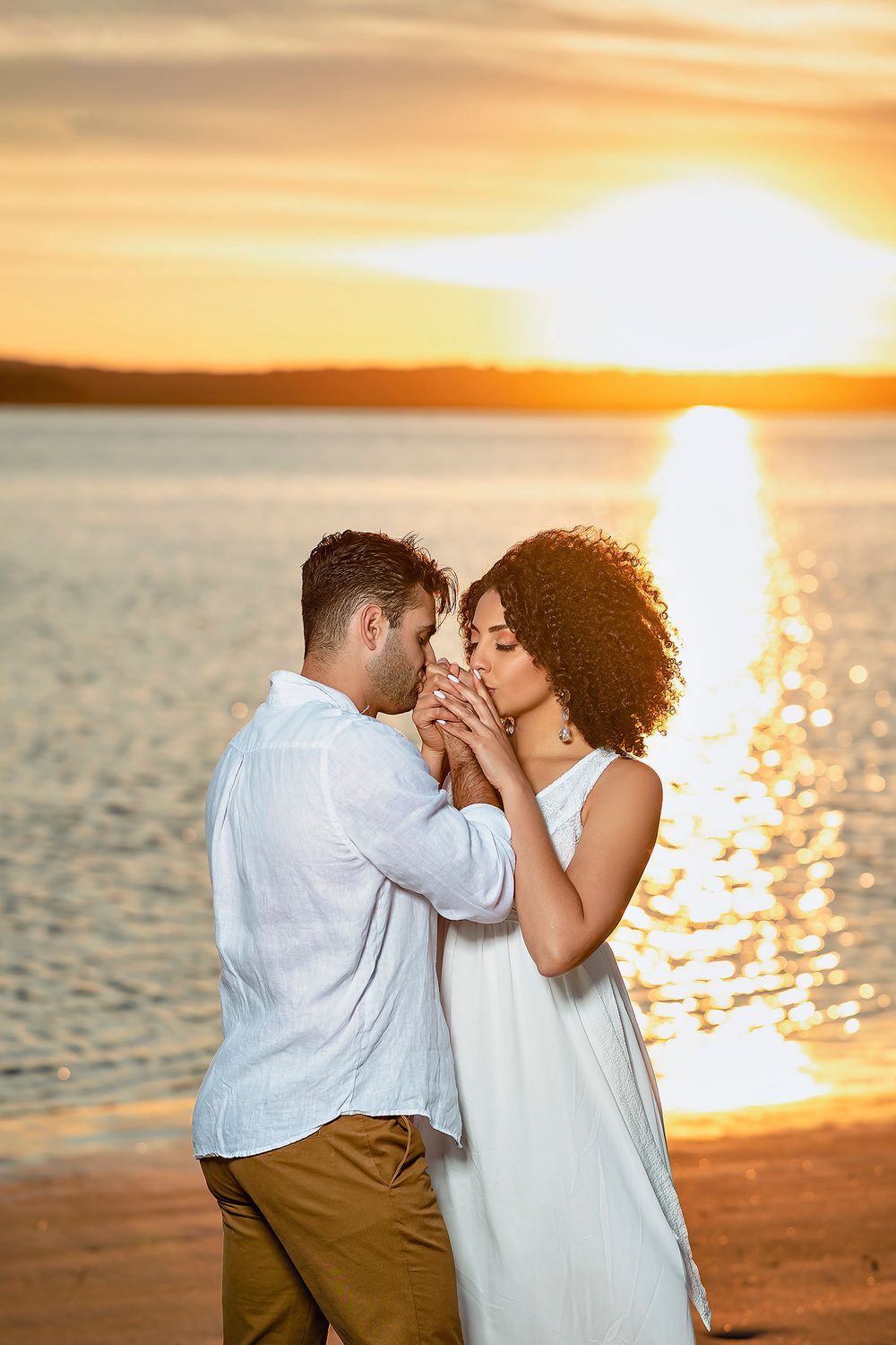 Intimate beach engagement photos at golden hour with couple in white and khaki against sunset.