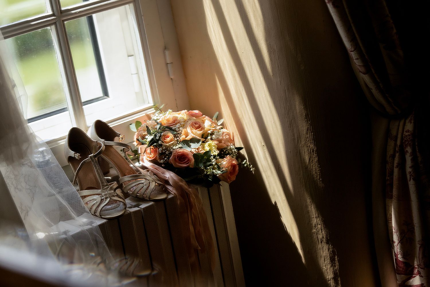 Wedding shoes and bouquet sit in natural window light creating romantic ambiance.
