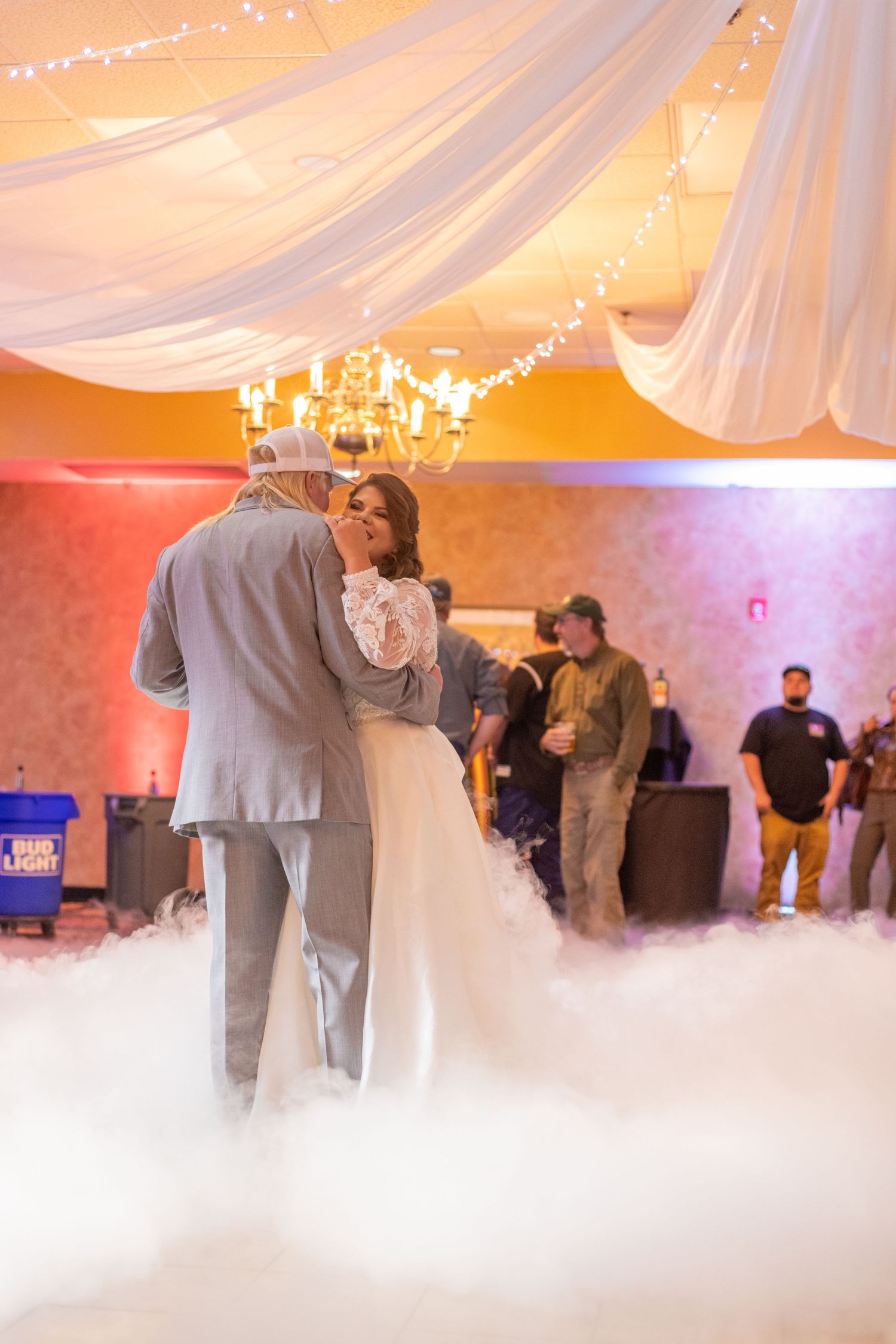 A couple shares their first dance in a beautifully decorated reception hall with fog effects and soft lighting.