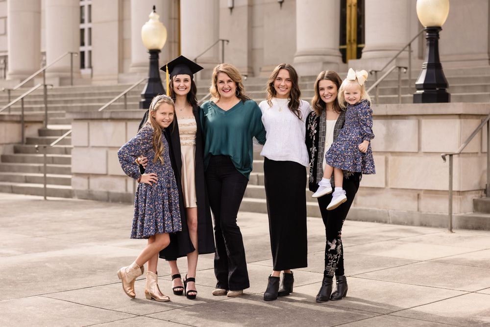 Group graduation photo with graduates posing on steps of classical building.