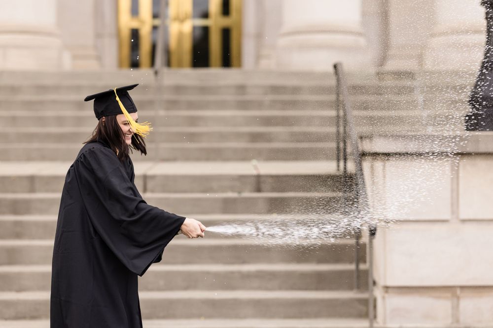 Graduate in cap and gown walking along classical building steps.