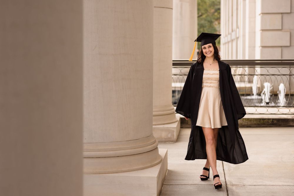 Graduation photoshoot featuring graduate in black cap and gown at columned building entrance.