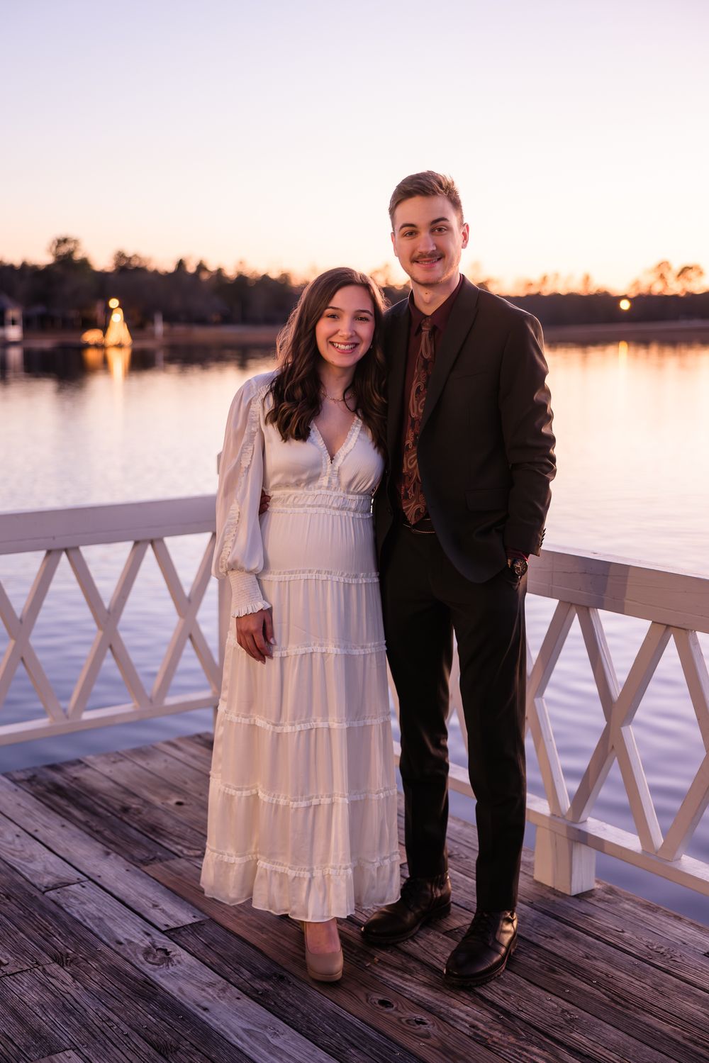 Sunset engagement photos of couple on wooden dock wearing white dress and dark suit.