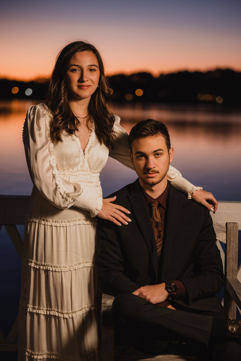 Moody sunset portraits of couple on waterfront dock with dramatic lighting.