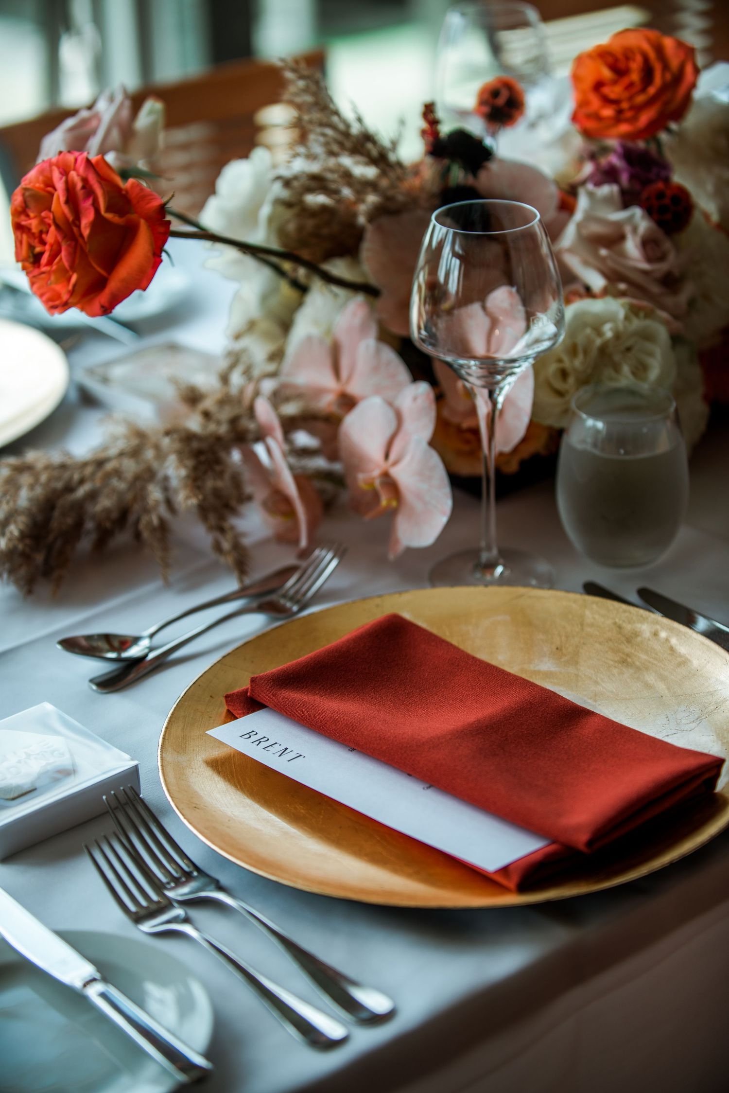 Place setting with gold charger plate, coral napkin and floral decorations at a wedding reception.