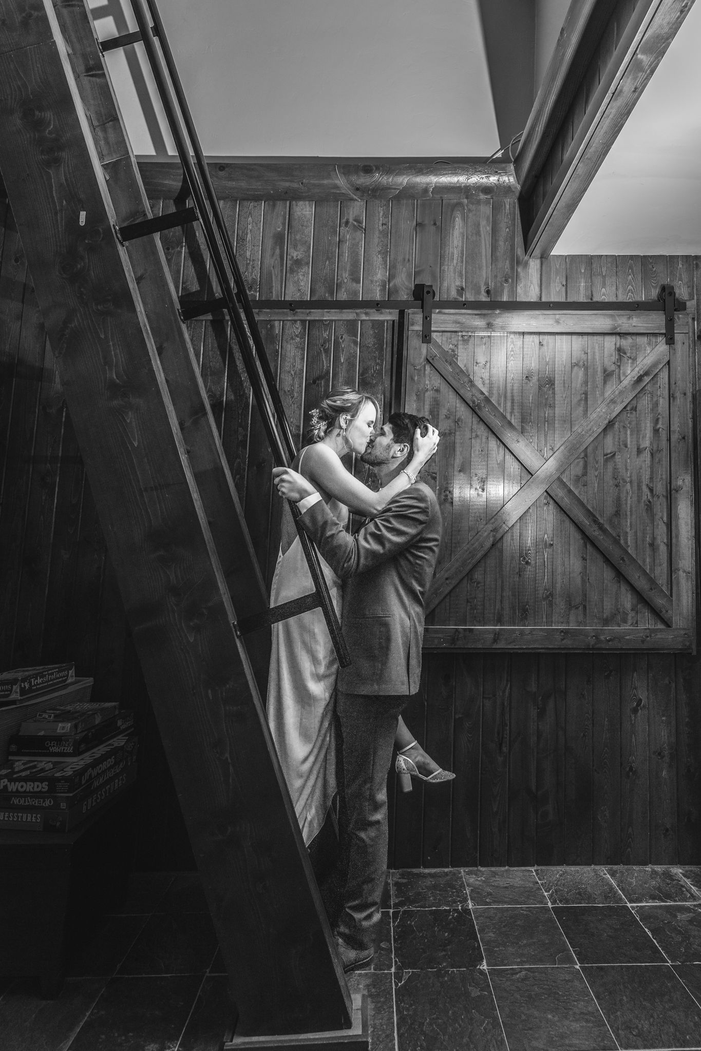 A dramatic black and white photo of a couple embracing near a wooden door and staircase.