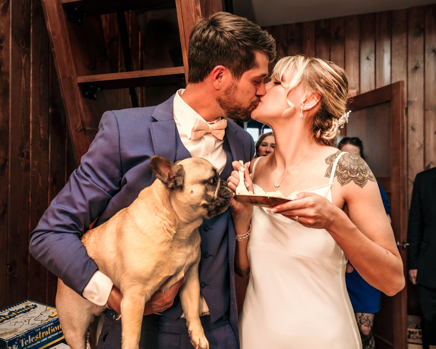 A couple shares a moment with their French Bulldog in a rustic setting.