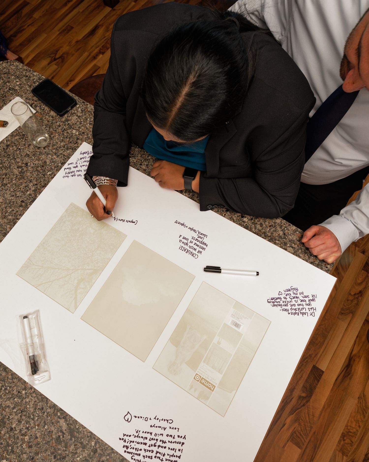 Someone signs documents and reviews architectural plans on a wooden floor.