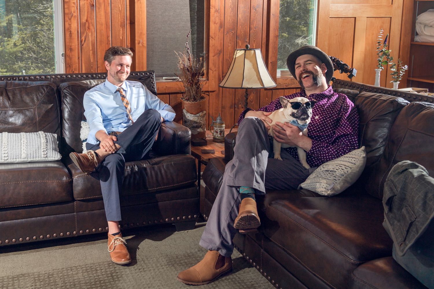 Two people relaxing on leather couches in a wood-paneled room.