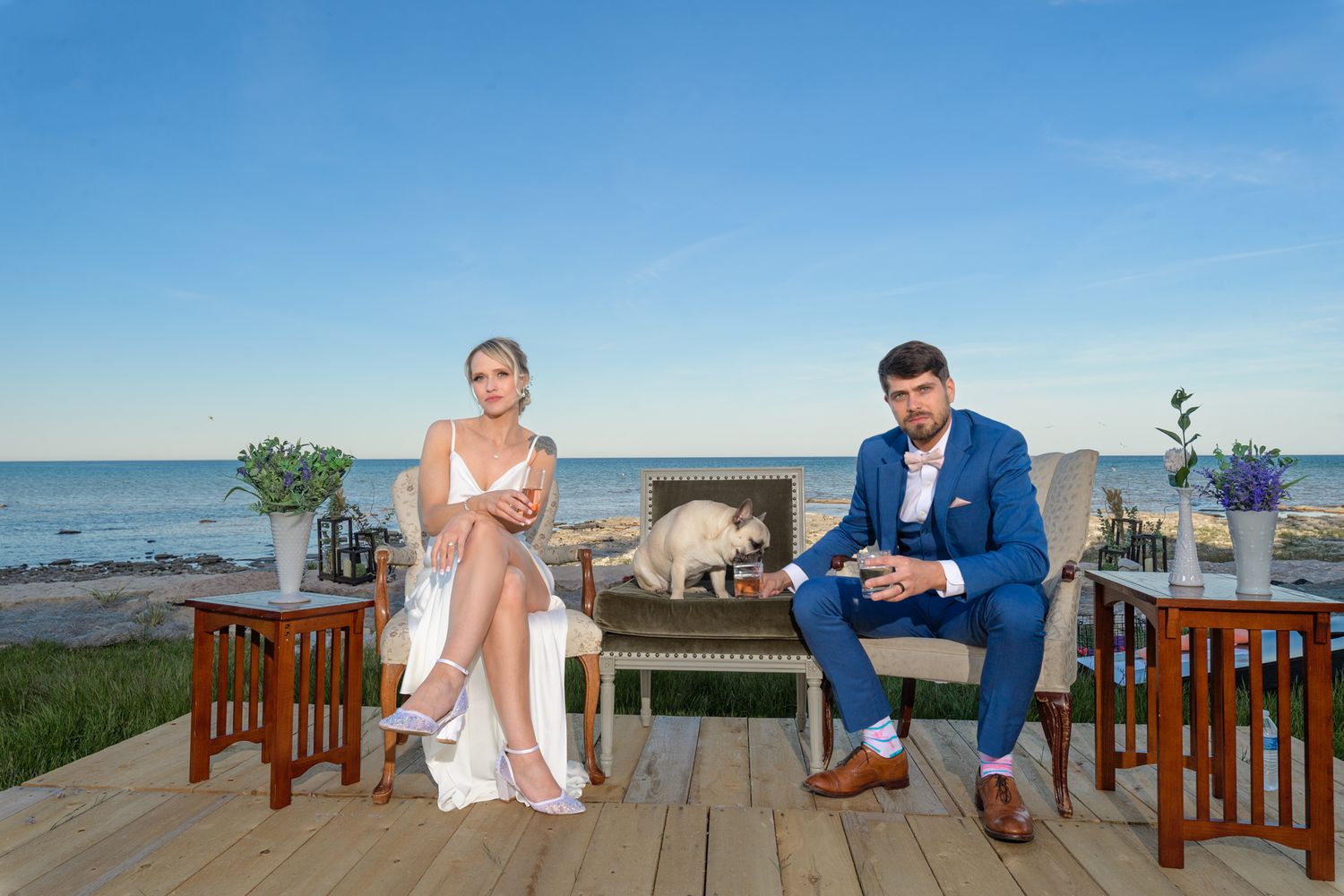 A couple sits on wooden chairs on a deck overlooking the ocean.