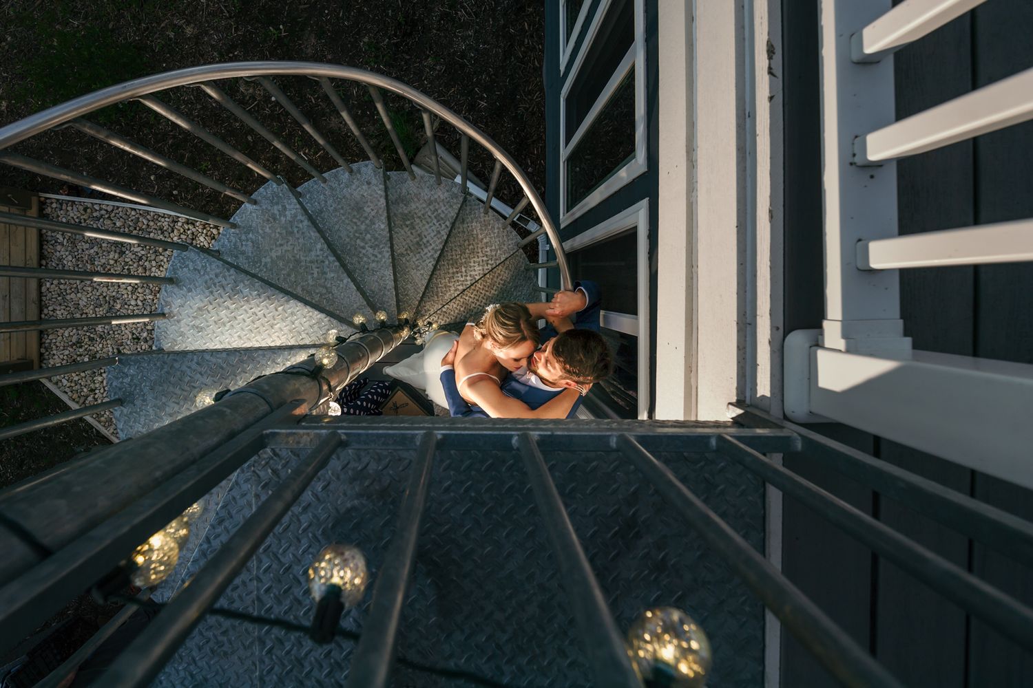 A couple poses together on a modern metal spiral staircase with dramatic lighting.