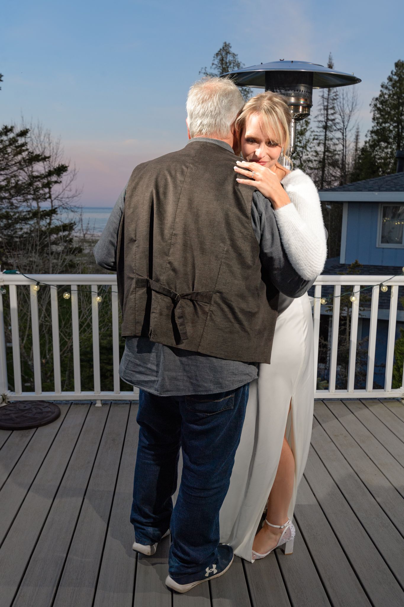 A tender moment captured on an outdoor deck with pine trees and water views in the background.