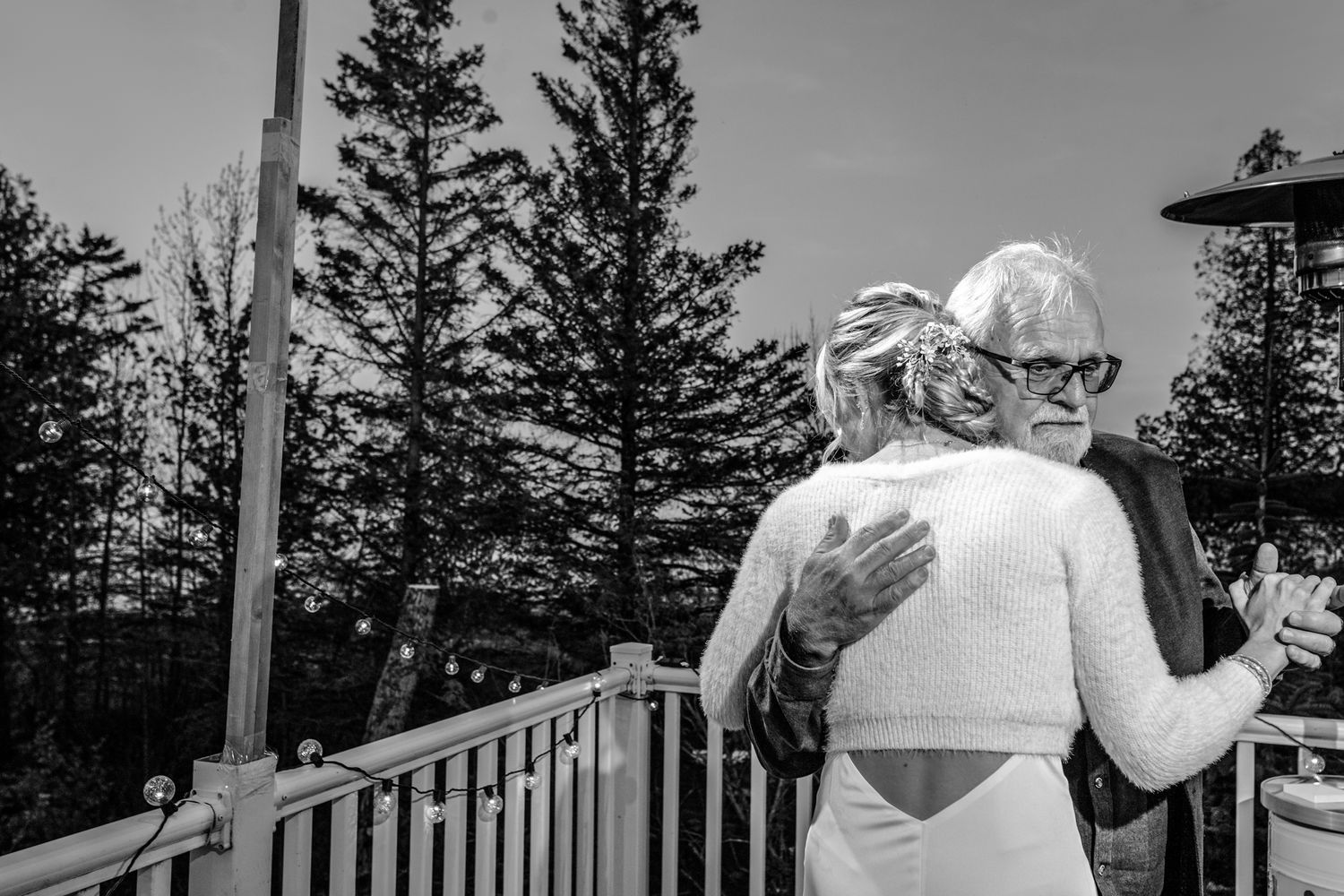 Black and white photo of an emotional moment shared on a deck surrounded by pine trees.
